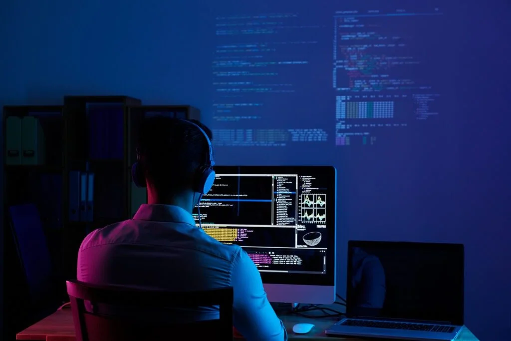 Programmer writing code at a dark multi-monitor desk.